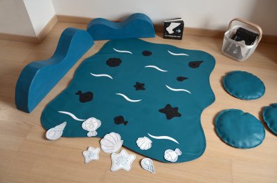 Tapis d'activités "Au bord de la mer" avec ses 8 animaux à mettre en place grâce à leur scratch et ses décors en volume de vagues.