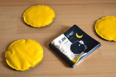 3 coussins-galettes bicolores jaunes et noirs et l'album en tissu fabriqués par l'autrice…