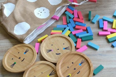4 galettes de bois, 90 pièces de bois rectangulaires de 6 couleurs différentes et 2 dés, rangés dans une sacoche en toile de jute à l'effigie de Camélion.