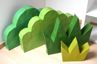 4 décors de végétaux en volume et carton peint, à disposer au sol pour mettre en scène le bord de la rivière avec les tapis, les galettes d'assise et le décor d'hippopotame.
