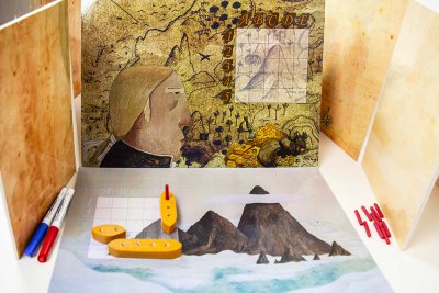 Niveau 1 - Vue des plateaux et grilles de tirs d'un des deux joueurs avec ses 3 navires dispos&eacute;s. "Sacrebleu ! Il a touch&eacute; ma go&eacute;lette !". Bateau touch&eacute; en case E1 (Pique rouge).