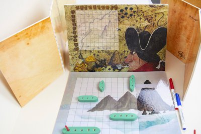 Niveau 2 - Vue des plateaux et grilles de tirs d'un des deux joueurs avec ses 5 navires dispos&eacute;s. "Cornebouc ! Il a touch&eacute; mon galion !". Bateau touch&eacute; en case A10 (Pique rouge).